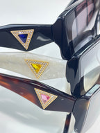 Prada sunglasses close-up of triangular jeweled logo on dark temple arm.