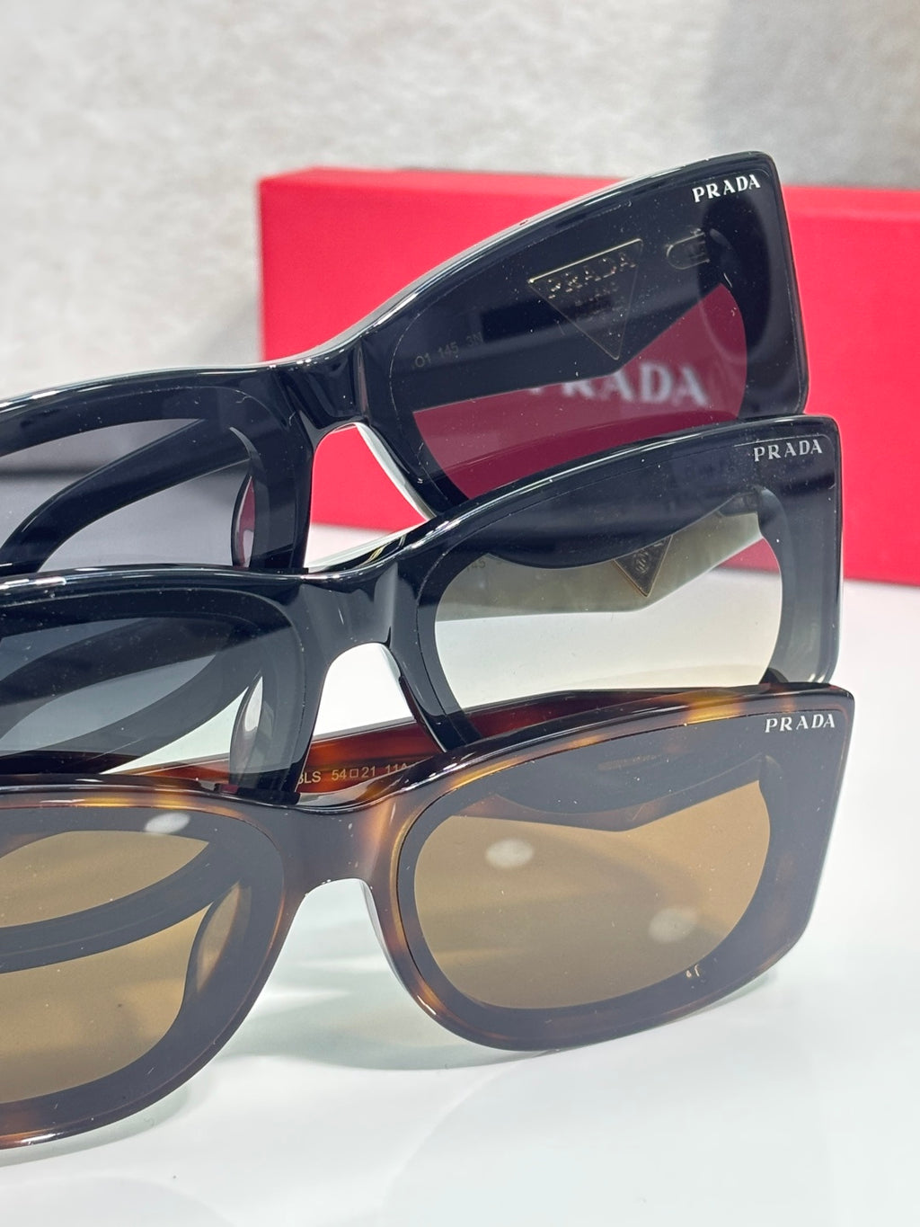 Prada sunglasses side view with logo on black temple and tortoise frame accents.