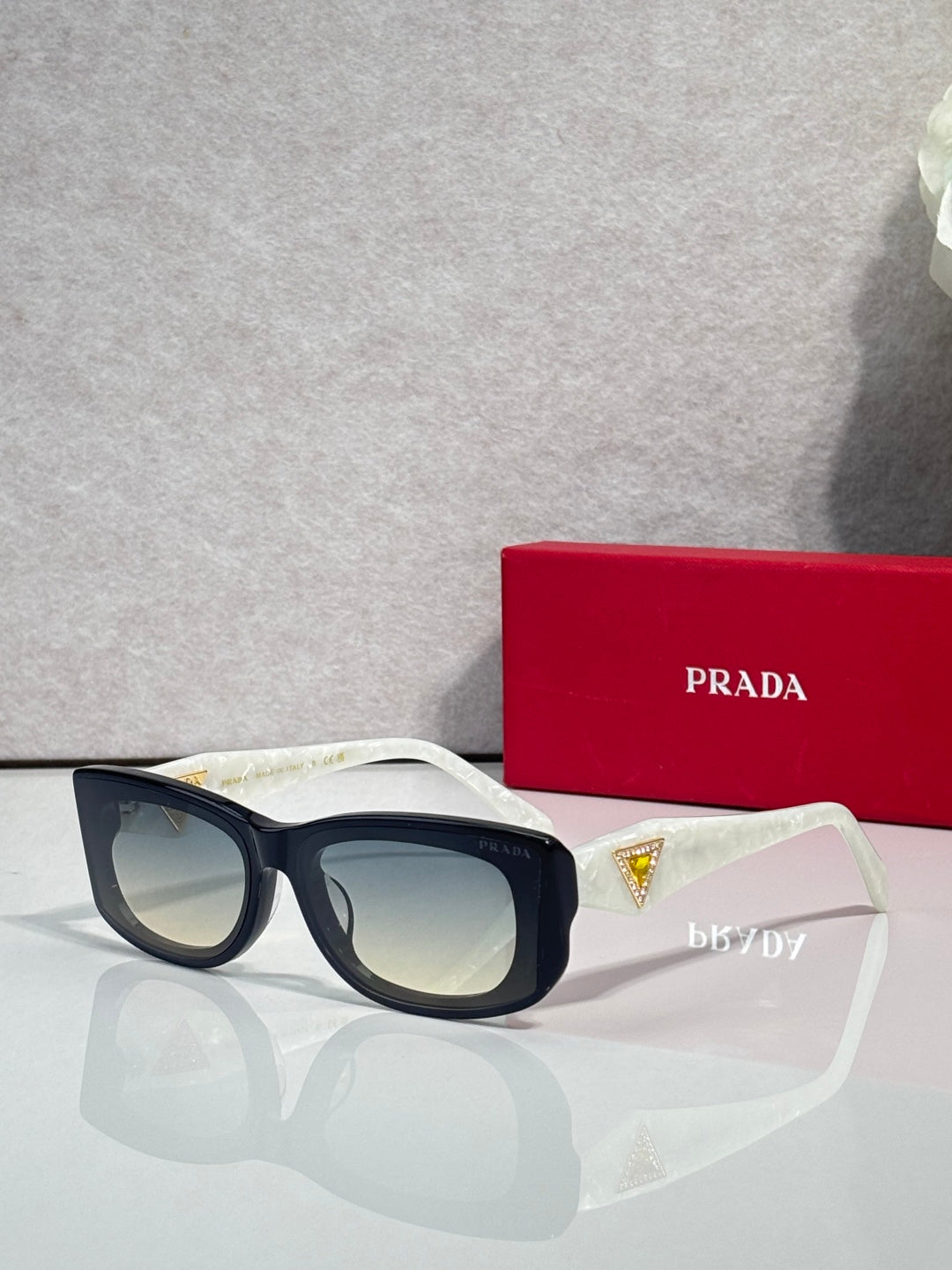 Prada sunglasses with light frames and pale lenses, triangular multicolor logo on side.