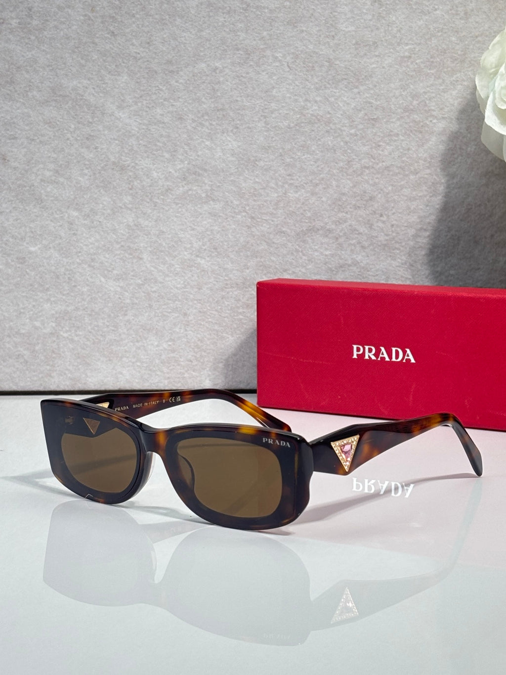 Prada sunglasses with tortoise-pattern frames and dark lenses, triangular logo on temple.