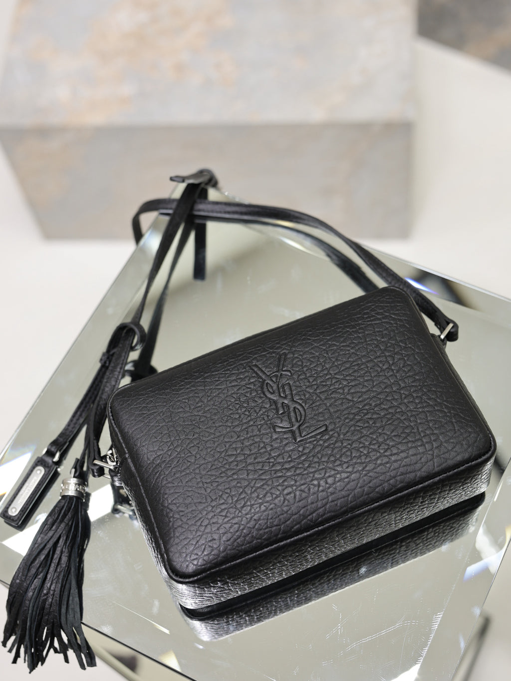 Black pebbled leather YSL crossbody bag with front logo and tassel side pull.