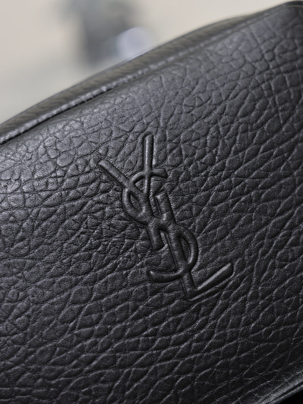 YSL logo embossed on black pebbled leather of a small crossbody bag.