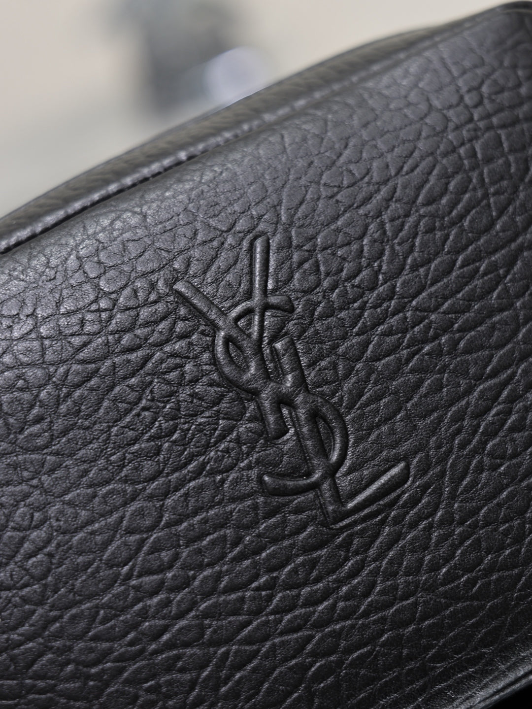 YSL logo embossed on black pebbled leather of a small crossbody bag.
