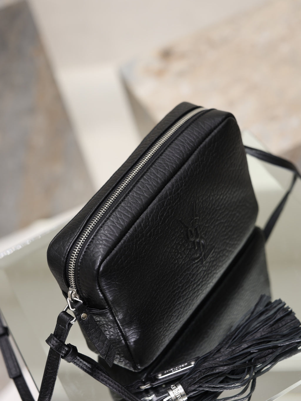 Black YSL zip-top crossbody bag with pebbled leather and tassel detail at the side.