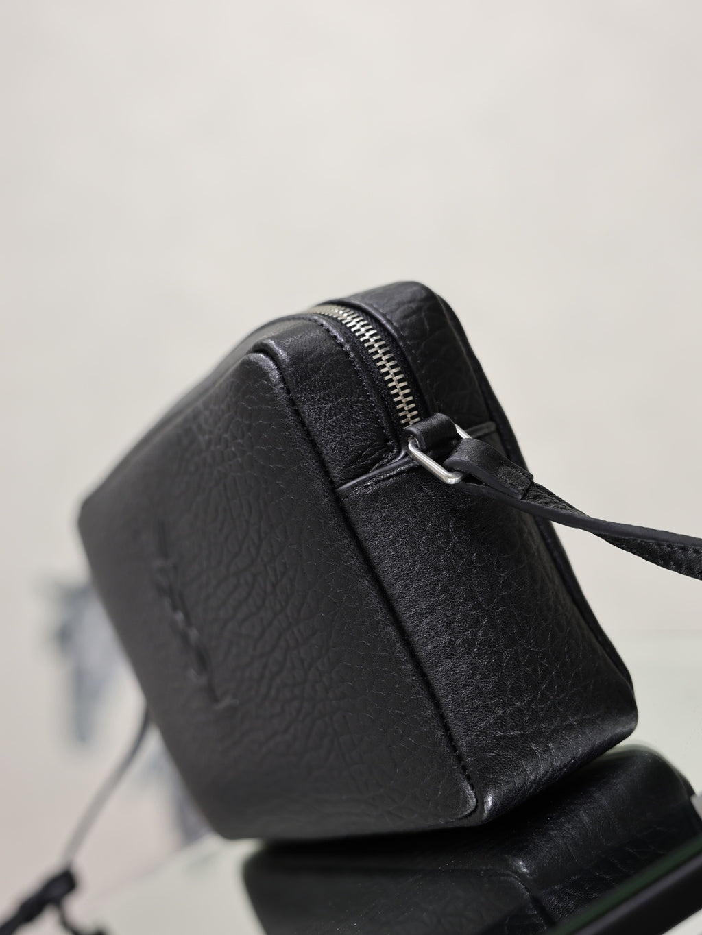 Black pebbled leather YSL crossbody bag with curved side and visible zip closure.