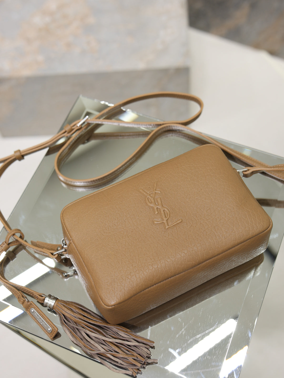 Tan leather YSL crossbody bag on display with embossed logo and tassel strap.