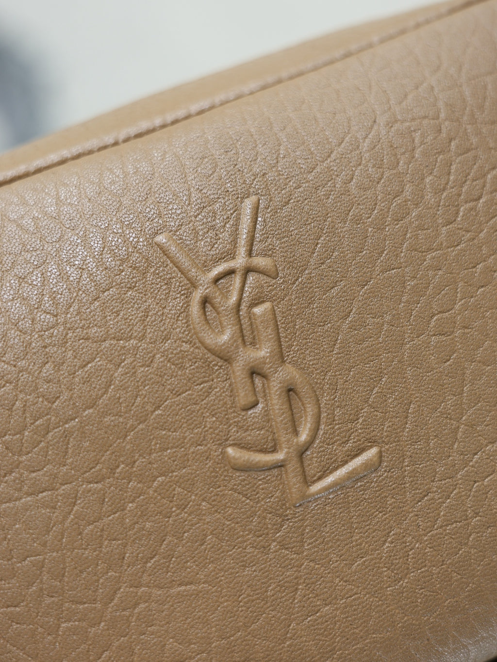 Tan textured leather bag close-up with embossed YSL monogram on the front.