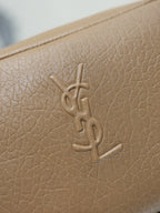 Tan textured leather bag close-up with embossed YSL monogram on the front.