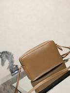 Tan YSL leather crossbody bag side view with zipper and tassel strap details.