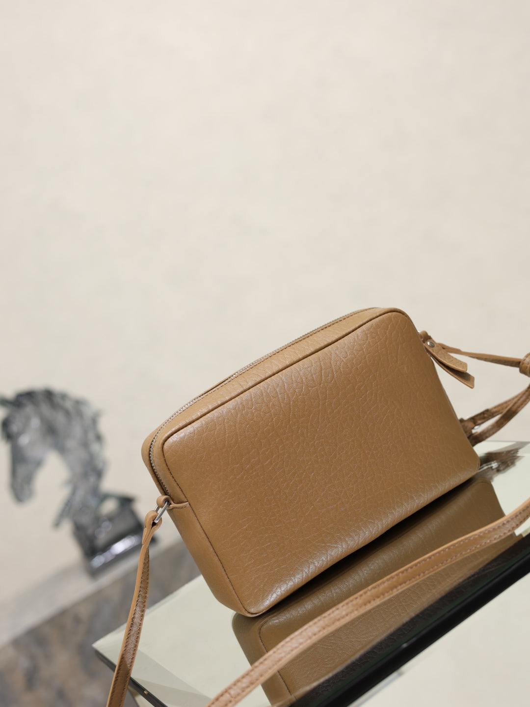 Tan YSL leather crossbody bag side view with zipper and tassel strap details.