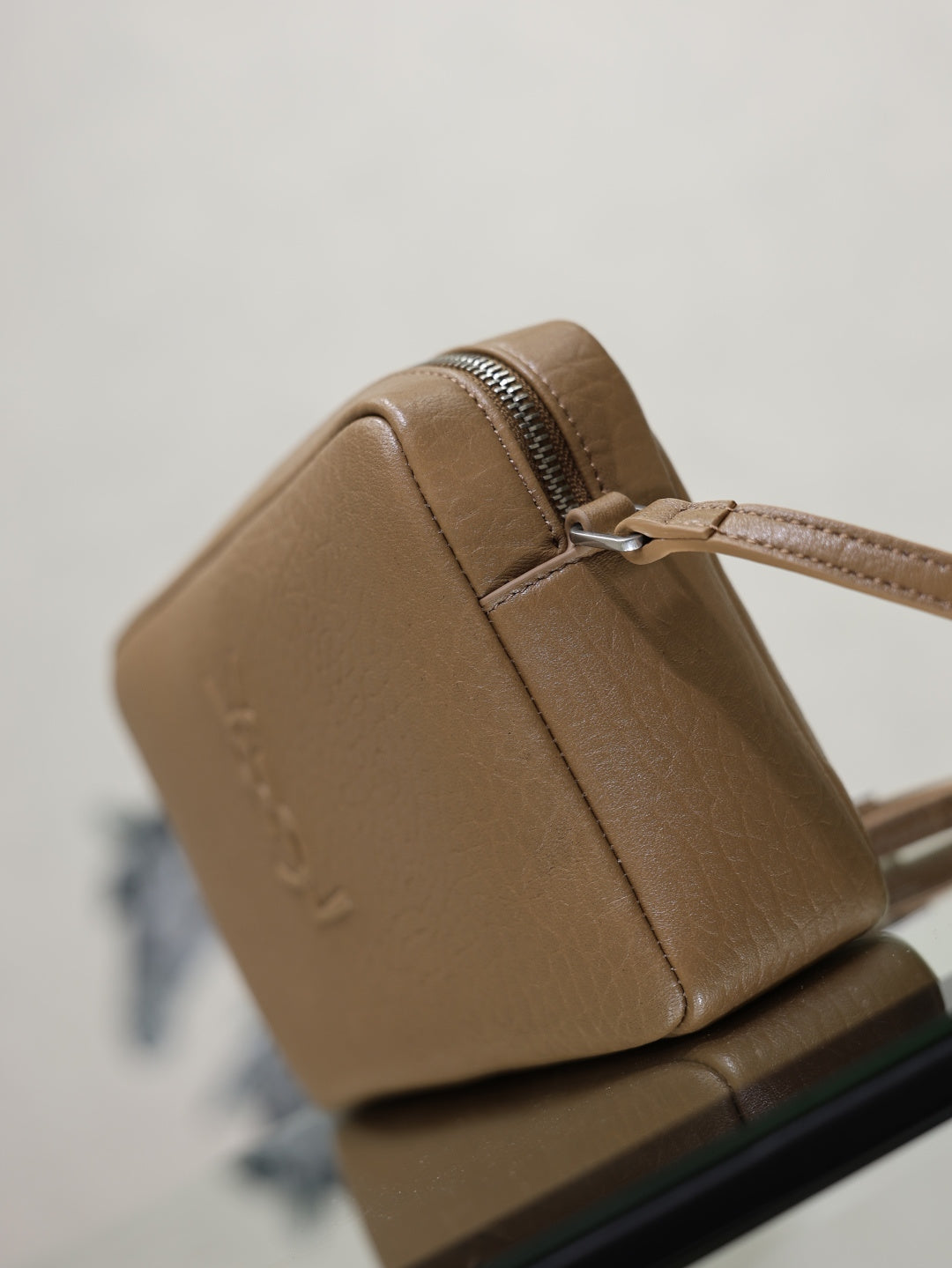 Tan leather YSL bag close-up showing zipper pull and stitched seams on the front.