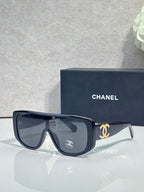 Sunglasses with dark frame and dark lenses, gold Chanel CC logo on temples.