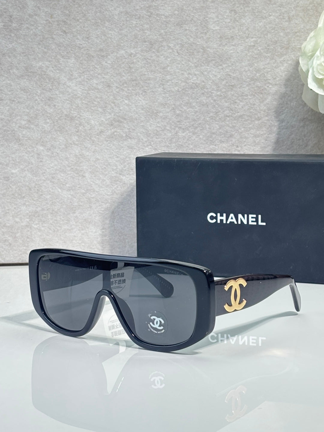 Sunglasses with dark frame and dark lenses, gold Chanel CC logo on temples.