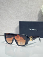 Sunglasses with dark frame and orange-tinted lenses, gold Chanel CC on temples.