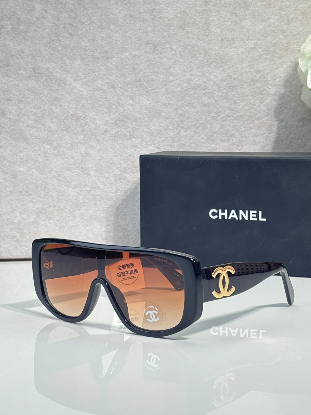 Sunglasses with dark frame and orange-tinted lenses, gold Chanel CC on temples.