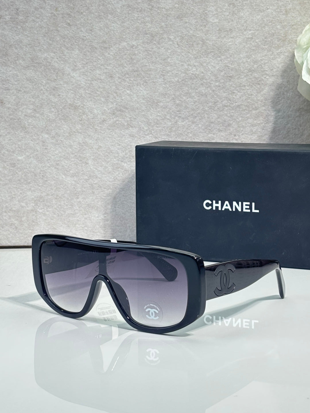 Sunglasses with dark navy frame, dark lenses, gold Chanel CC logos on temples.