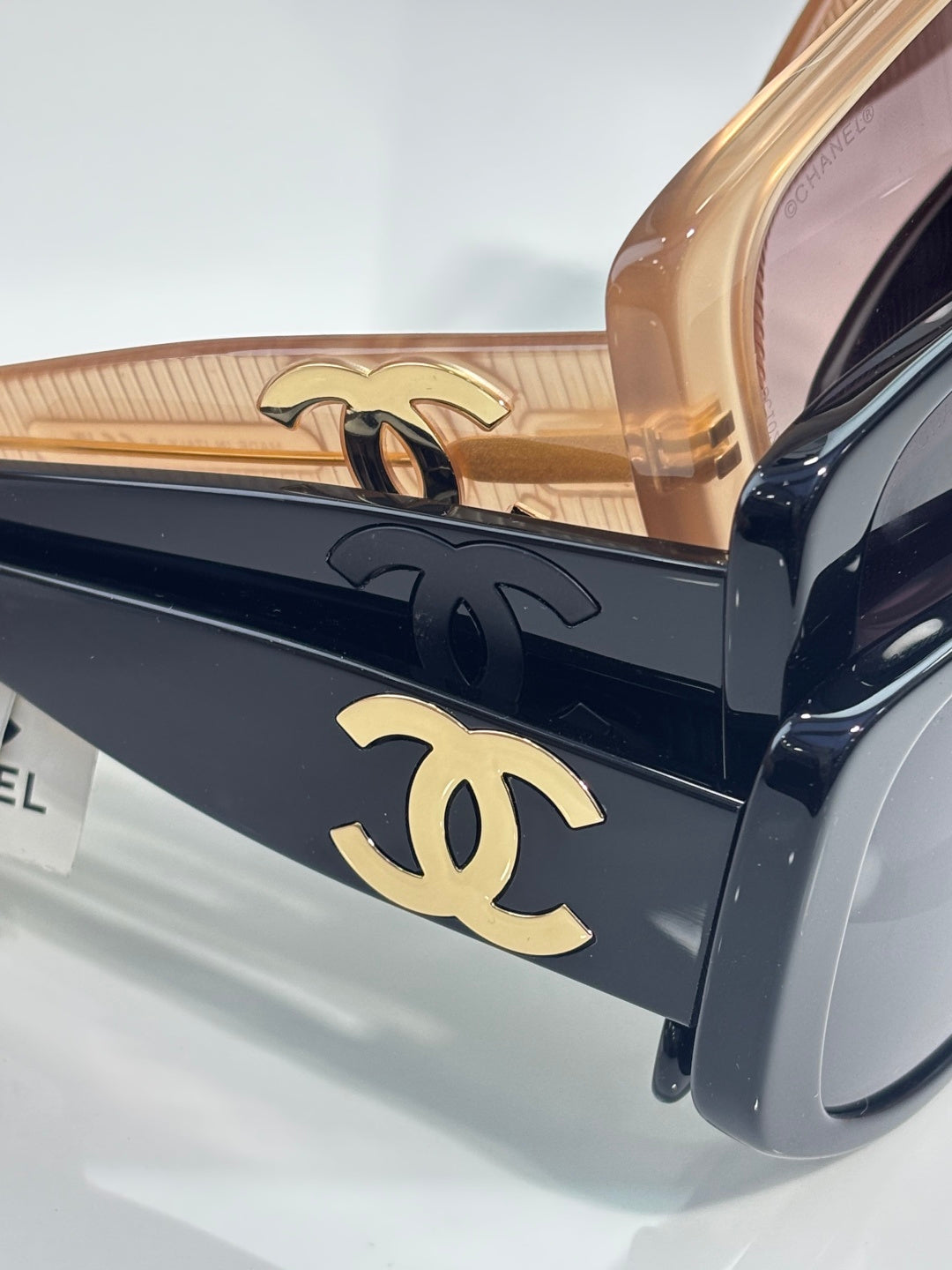 Sunglasses side close-up: dark frame with gold Chanel CC emblem on angular arms.
