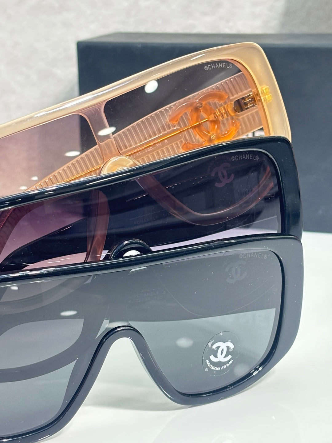 Chanel sunglasses close-up with dark lenses, tan accents, and gold Chanel CC details.