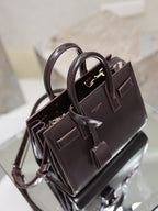 Dark brown leather handbag with double handles, crossbody strap, and gold hardware