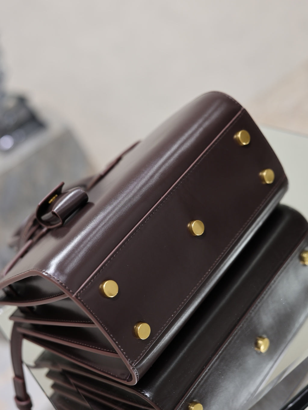 Dark brown leather handbag side view with gold snap buttons and top handle attachment