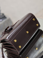 Dark brown leather handbag side view with gold snap buttons and top handle attachment