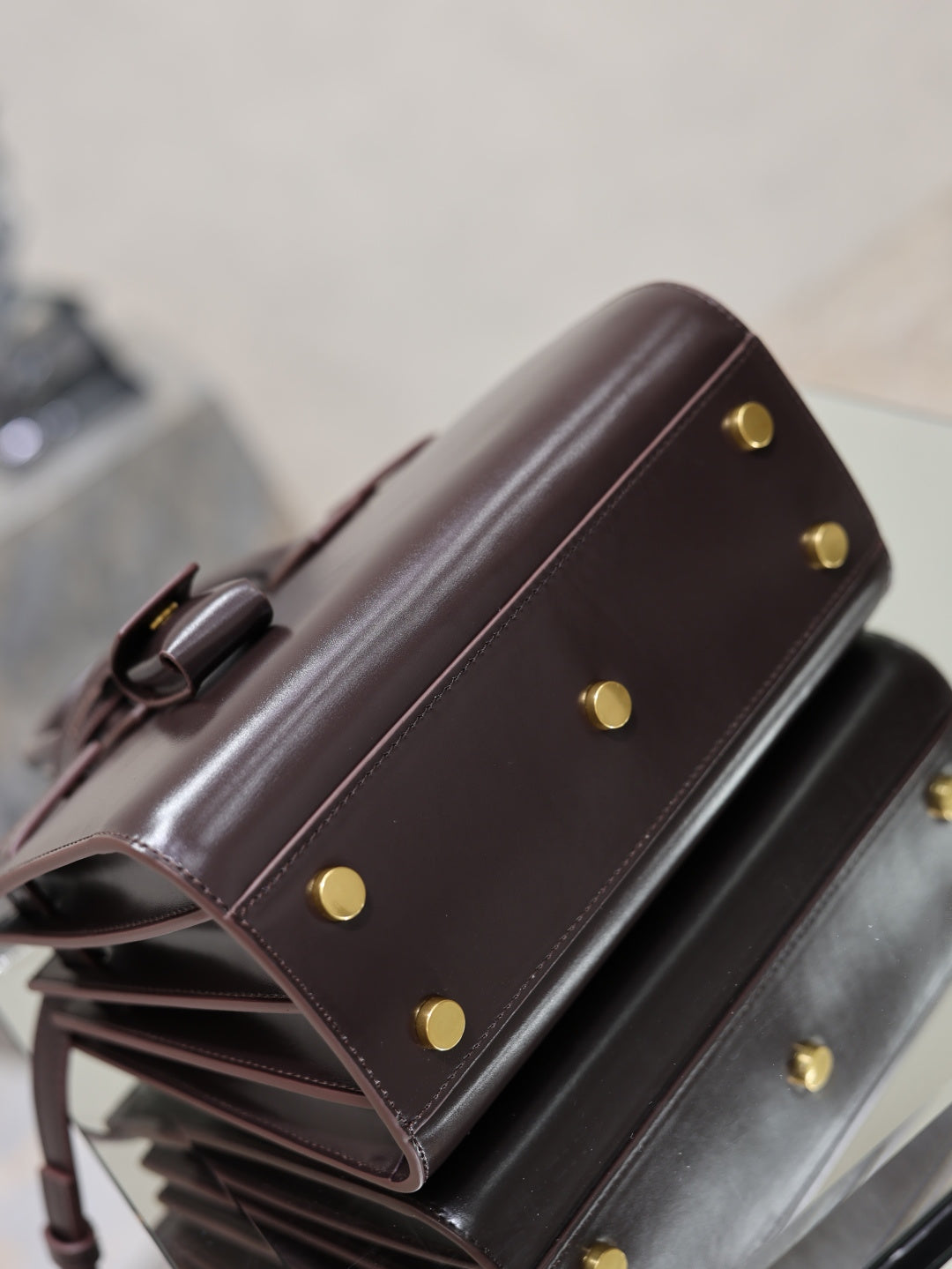 Dark brown leather handbag side view with gold snap buttons and top handle attachment