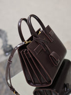 Dark brown leather handbag angled view with top straps, gold hardware, and pleated interior