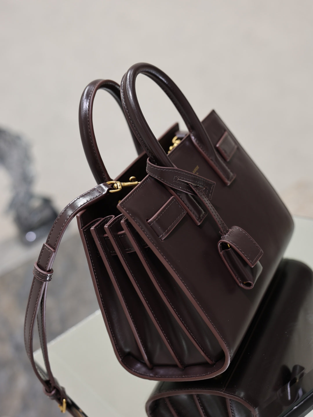 Dark brown leather handbag angled view with top straps, gold hardware, and pleated interior