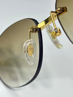 Gold-tone sunglasses side view with dark temple and oval lens logo detail