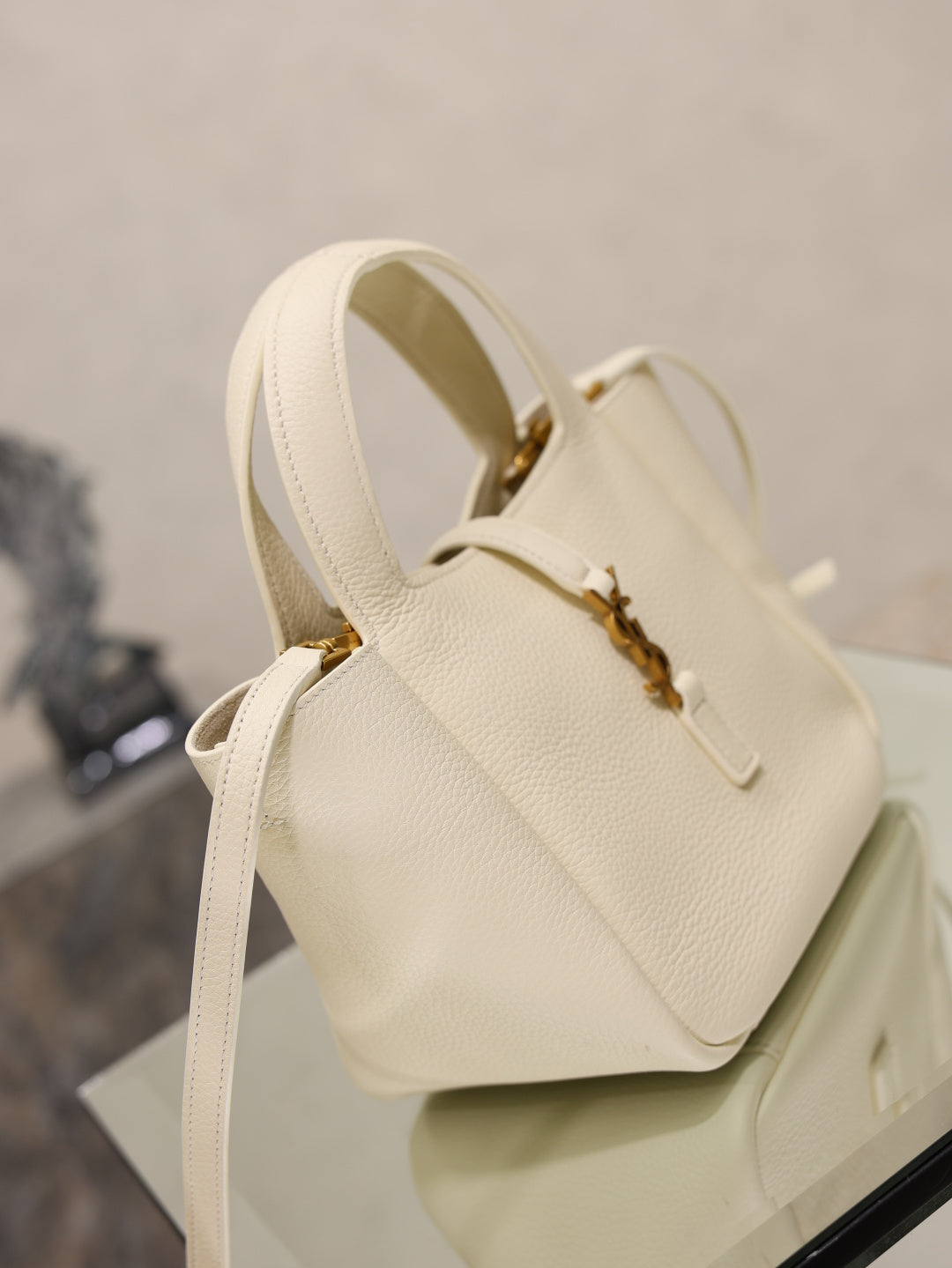 YSL bag in cream leather with gold hardware, adjustable crossbody strap and rounded top profile.