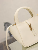 YSL bag close-up in cream leather with gold front clasp and top handle bar, textured grain.