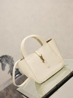 YSL bag in cream leather with gold clasp, short handles and crossbody strap, angled view.
