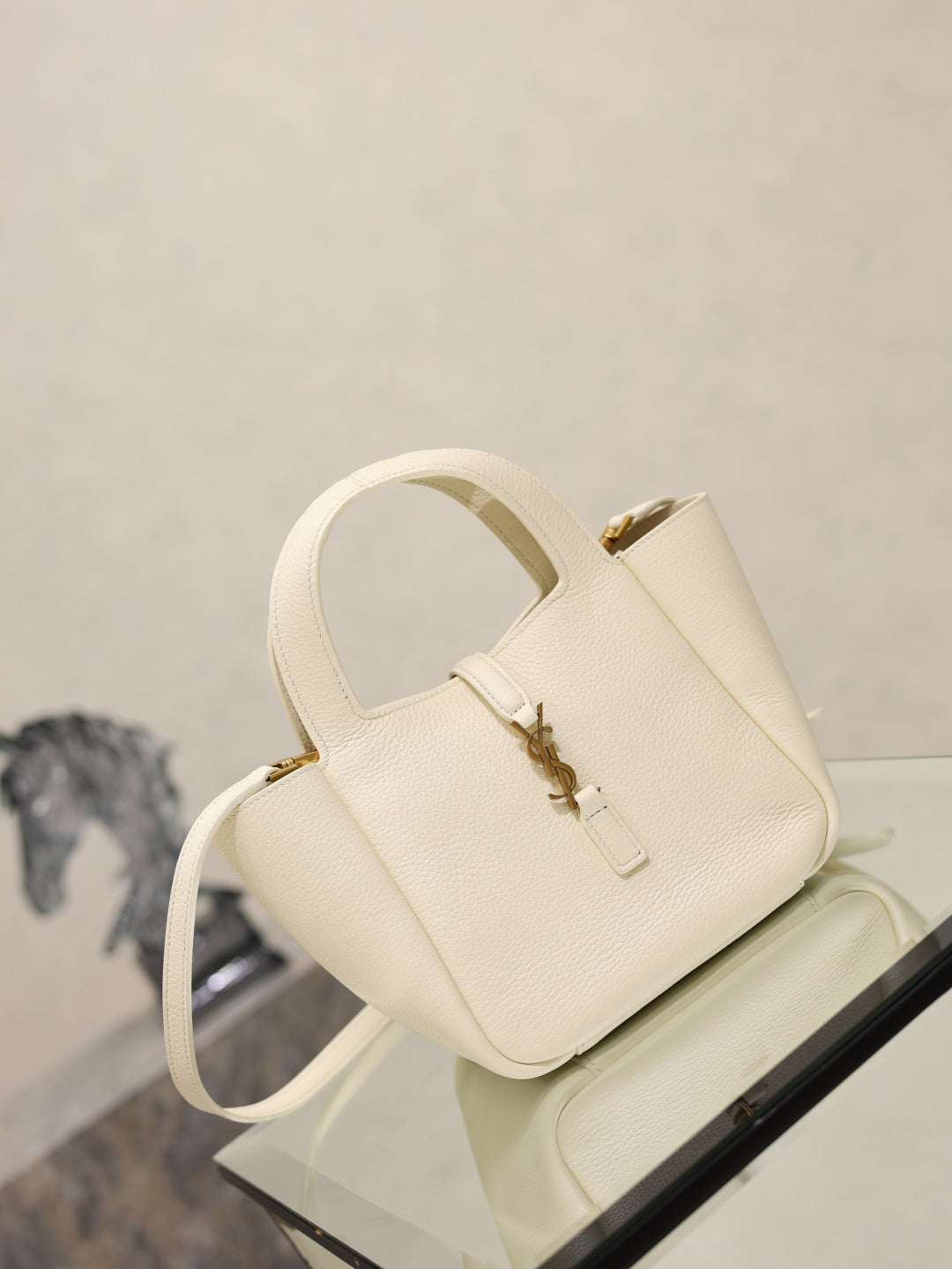 YSL bag in cream leather with gold clasp, short handles and crossbody strap, angled view.