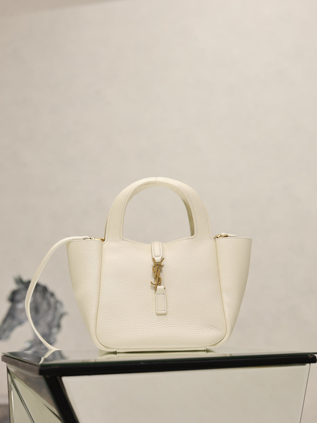 YSL bag in cream leather with gold clasp and top handles, structured mini silhouette.