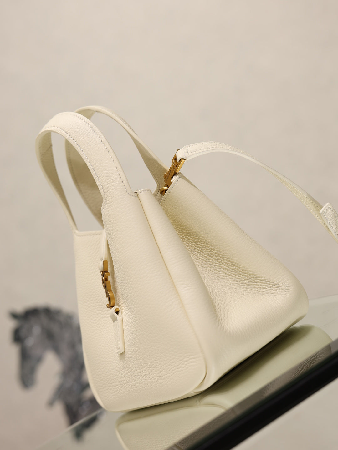 YSL bag in cream leather with gold clasp and vertical seam details, side view.