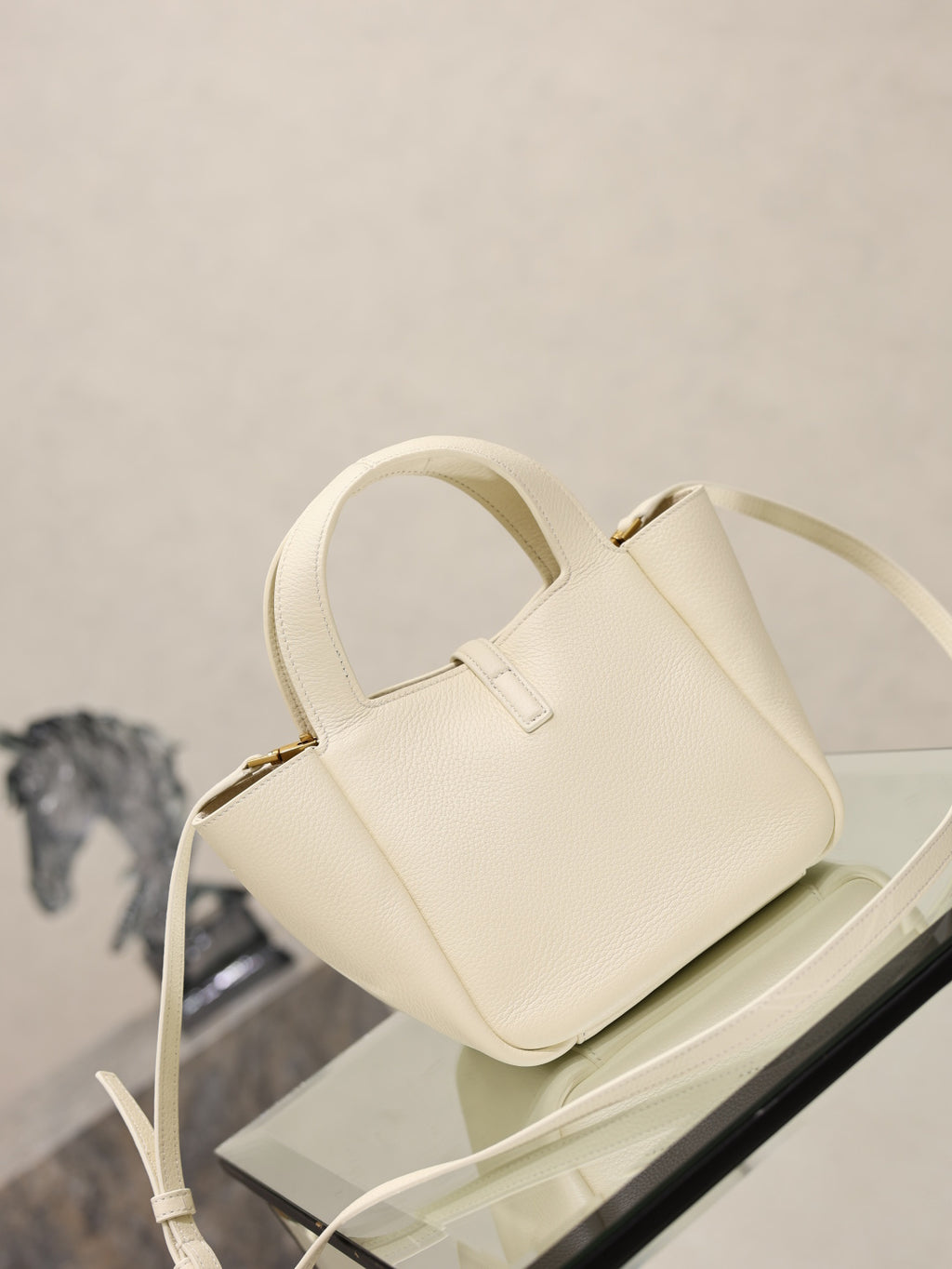 YSL bag in cream leather with gold clasp, top handle and long strap, three-quarter view.