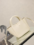 YSL bag in cream leather with gold clasp, top handle and long strap, three-quarter view.