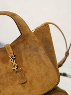 Tan suede mini tote close-up of YSL logo charm and top handle.