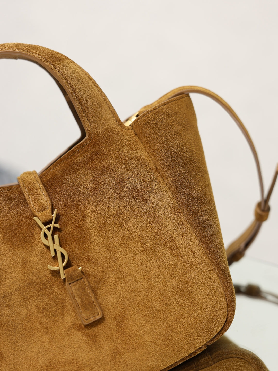 Tan suede mini tote close-up of YSL logo charm and top handle.