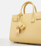 Light yellow tote bag front with top handles and dangling luggage tag charm