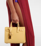 Light yellow structured tote bag held by top handles; gold-tone hardware visible