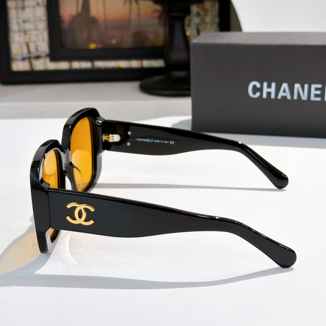 Black sunglasses side view with gold CC logo on temple and orange lenses.