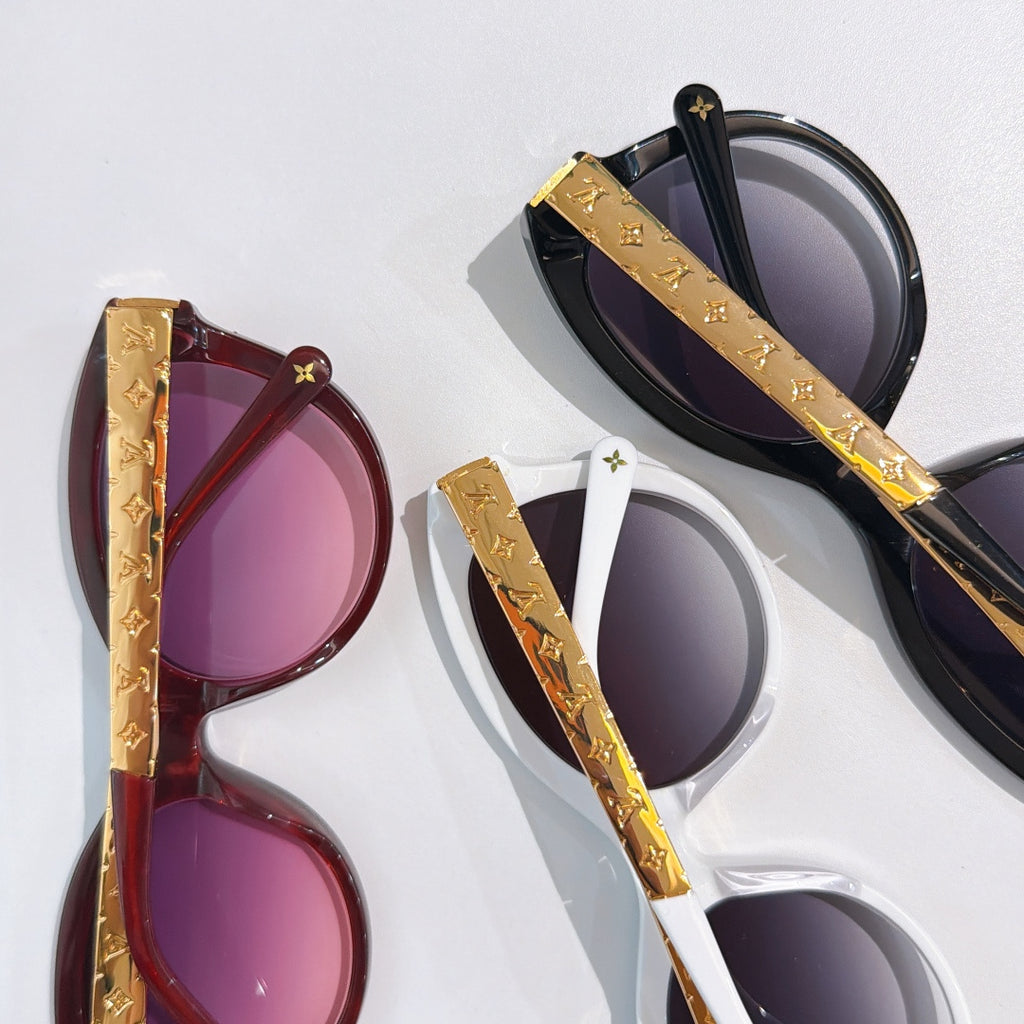 Pair of oval sunglasses with gold logo temples, one black and one burgundy, purple lenses