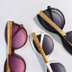 Pair of oval sunglasses with gold logo temples, one black and one burgundy, purple lenses