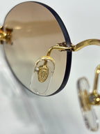 Close-up of dark lens sunglasses with gold-tone hinge and circular side emblem