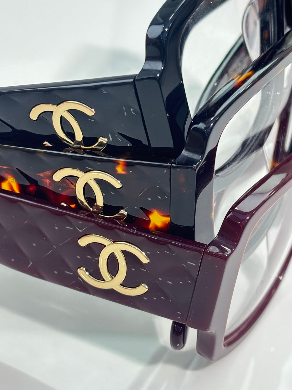 Close-up of patterned dark purple eyeglasses with gold CC logos on the top bar