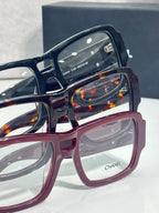Close-up of navy and burgundy rectangular eyeglasses with CHANEL logo on lenses