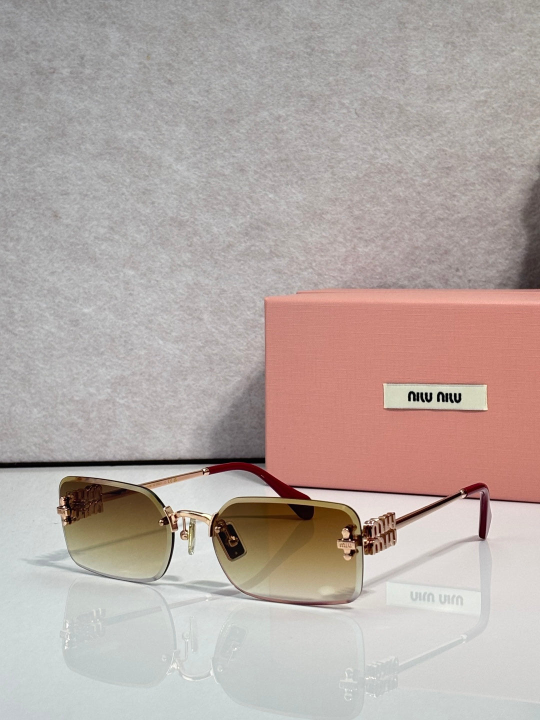 Sunglasses with brown-tinted lenses, gold frame, maroon accents on arms