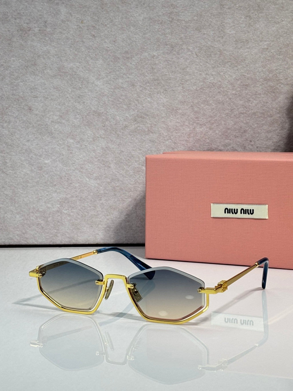 Gold-tone sunglasses with light blue lenses and black arms, rectangular cat-eye style.