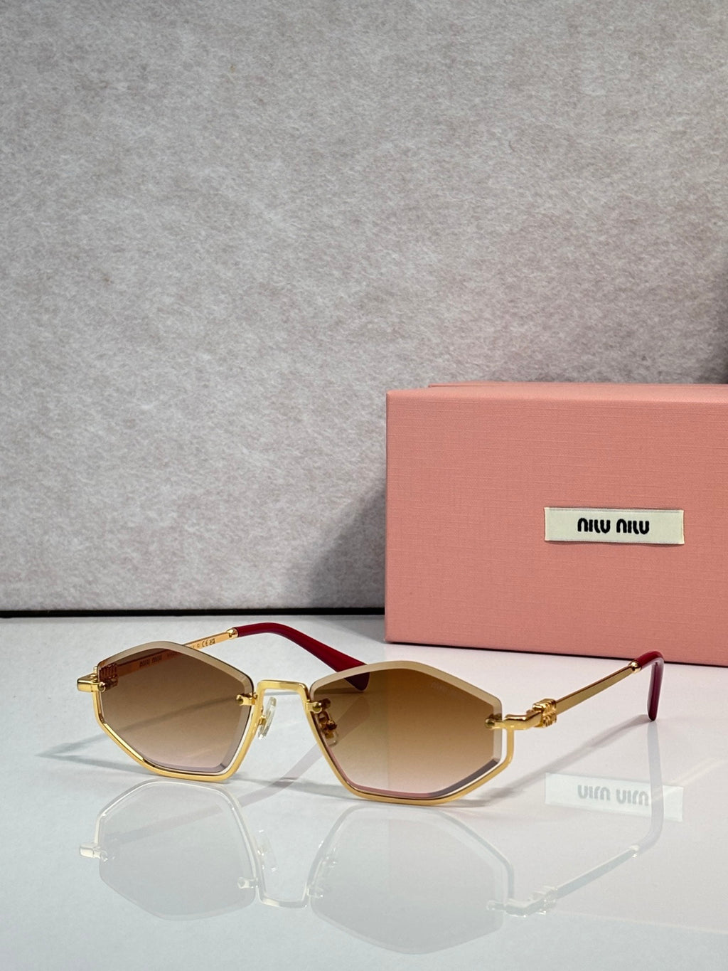 Gold-tone sunglasses with amber lenses and red-tinted arms, rectangular cat-eye style.